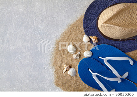 Straw hat, flip flops and seashells on scattered sea sand 90030300