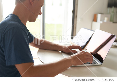 A young man sitting at home in front of a laptop. A serious person working remotely at home. High quality photo A young man sitting at home in front of a laptop. A serious person working remotely at home. High quality photo 90030499