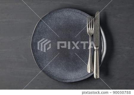 Dark plate on a dark concrete background with cutlery Dark plate on a dark concrete background with cutlery 90030788