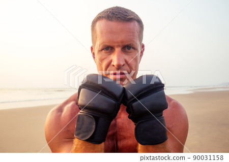 Strong boxer man doing during kickboxing exercise fight with trainer at sunset .close portrait of handsome fitness male model bodybuilder rage, anger and a splash of negative emotions Strong boxer man doing during kickboxing exercise fight with trainer at sunset .close portrait of handsome fitness male model bodybuilder rage, anger and a splash of negative emotions 90031158