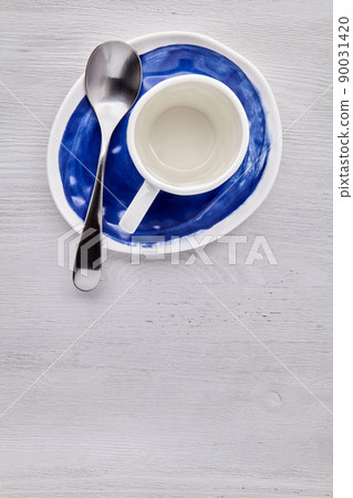 Empty white cup for hot drinks with a spoon on a blue plate Empty white cup for hot drinks with a spoon on a blue plate 90031420