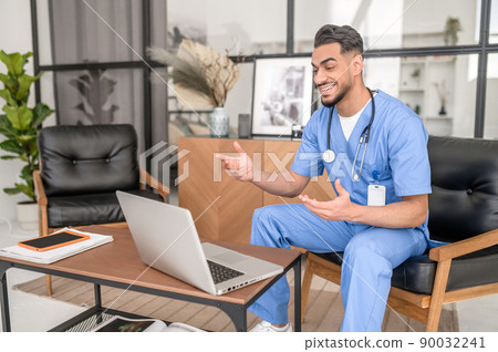 Joyful young doctor consulting his patient online 90032241
