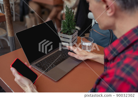 Man sitting with smartphone touching laptop Man sitting with smartphone touching laptop 90032302