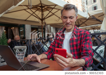 Man looking at smartphone sitting at laptop Man looking at smartphone sitting at laptop 90032303