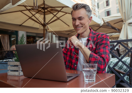 Man looking at laptop sitting in outdoor cafe Man looking at laptop sitting in outdoor cafe 90032329