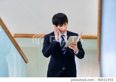 A businessman talking on a smartphone with a notebook in one hand A businessman talking on a smartphone with a notebook in one hand 90032393