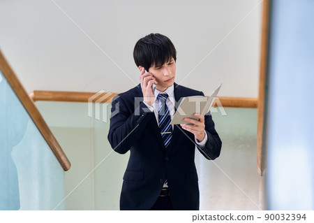 A businessman talking on a smartphone with a notebook in one hand A businessman talking on a smartphone with a notebook in one hand 90032394