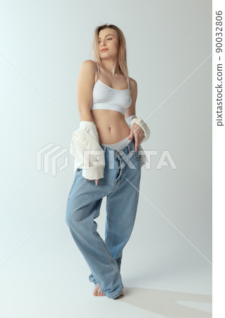 Full-length portrait of young slim girl wearing shirt, underwear and jeans isolated over grey studio background Full-length portrait of young slim girl wearing shirt, underwear and jeans isolated over grey studio background 90032806