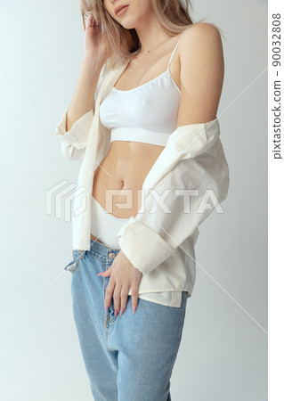 Cropped portrait of young slim girl wearing shirt, underwear and jeans isolated over grey studio background. Naturality Cropped portrait of young slim girl wearing shirt, underwear and jeans isolated over grey studio background. Naturality 90032808