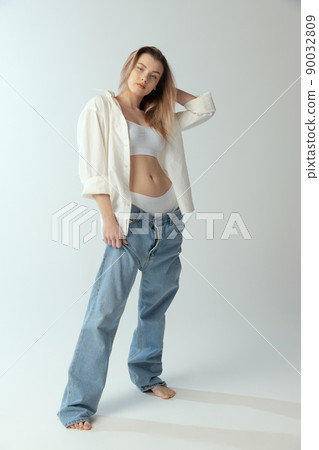 Full-length portrait of young slim girl wearing shirt, underwear and jeans isolated over grey studio background. Youth beauty Full-length portrait of young slim girl wearing shirt, underwear and jeans isolated over grey studio background. Youth beauty 90032809