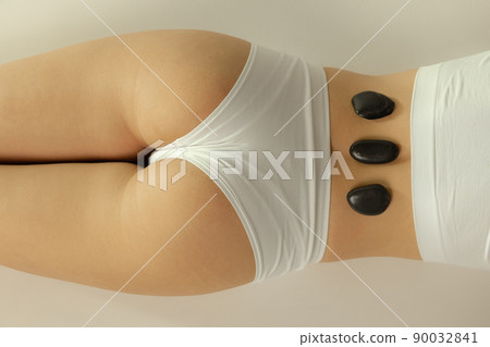 Cropped image of female body in underwear with warm stones on it isolated over grey studio background. Stone massage treatment Cropped image of female body in underwear with warm stones on it isolated over grey studio background. Stone massage treatment 90032841