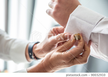 Best man helping groom fix cufflinks on his shirt before the wedding ceremony 90032910