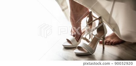 Bride puts her foot into white high heel shoe before the start of a wedding ceremony Bride puts her foot into white high heel shoe before the start of a wedding ceremony 90032920