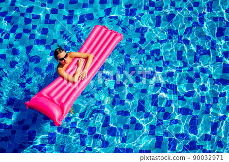 copy space spf and sunscreen beautiful brunette girl floating in the pool water.woman swimming and relaxing on pink inflatable mattress in blue swimmingpool remote work and freelance top view 90032971