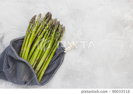 Fresh raw green asparagus spears in eco-friendly reusable produce bag on gray background, copy space 90033518