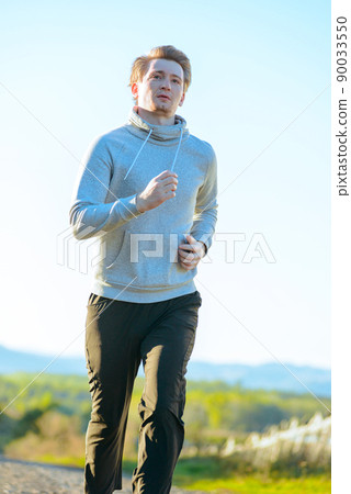 Man jogging in rural nature at beautiful summer day. Sport fitness model caucasian ethnicity training outdoor. 90033550