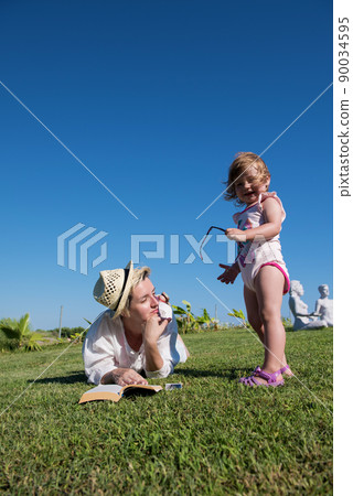 Woman lying and reading her favorite book on a meadow covered with fresh green grass on a sunny summer or spring day. 90034595