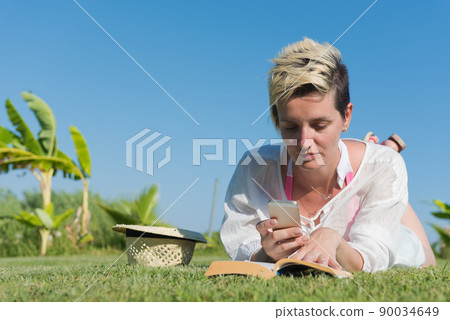 Woman lying and reading her favorite book on a meadow covered with fresh green grass on a sunny summer or spring day. Woman lying and reading her favorite book on a meadow covered with fresh green grass on a sunny summer or spring day. 90034649