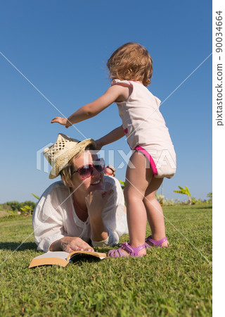 Woman lying and reading her favorite book on a meadow covered with fresh green grass on a sunny summer or spring day. Woman lying and reading her favorite book on a meadow covered with fresh green grass on a sunny summer or spring day. 90034664