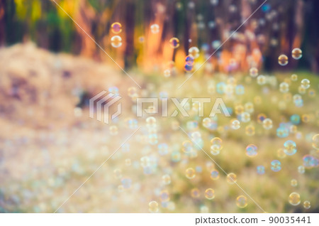 Abstract blurred of rainbow soap bubbles from the bubble blower flying on green grass. spring or summer season background. symbol of childhood. bokeh background. Abstract blurred of rainbow soap bubbles from the bubble blower flying on green grass. spring or summer season background. symbol of childhood. bokeh background. 90035441