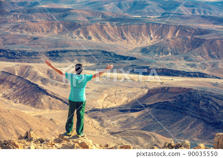 A man with hands in the air standing on the cliff in the desert A man with hands in the air standing on the cliff in the desert 90035550