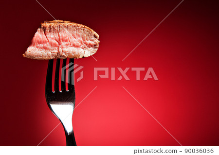 Piece of a grilled steak on a fork isolated on red 90036036