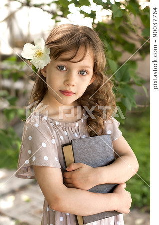 A charming little girl in a summer park with her eyes closed and a book in her hands. The concept of a happy life 90037764