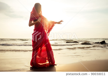 indian female model in vacation on paradise tropical beach by ocean sea. hindu woman with kundan jewelry traditional India costume red wedding sari.asian girl near the rocks shores of Indian Ocean bay 90038011