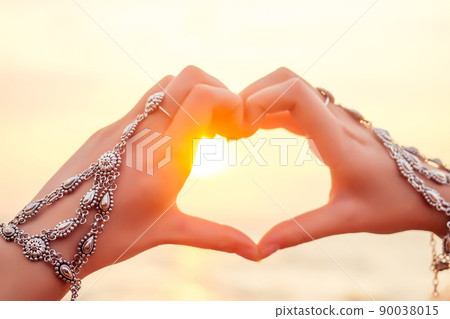 Female hands in the form of heart against the sky pass sun beams. Hands in a luxurious double silver jewelry bracelet and ring East style in shape of love heart Indian Ocean sunset Valentine's Day Female hands in the form of heart against the sky pass sun beams. Hands in a luxurious double silver jewelry bracelet and ring East style in shape of love heart Indian Ocean sunset Valentine's Day 90038015