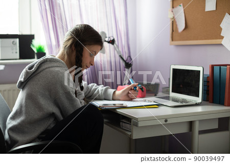 A student is sitting at her desk doing schoolwork. A student is sitting at her desk doing schoolwork. 90039497