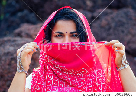portrait of attractive indian female model in vacation on paradise tropical beach by ocean sea. hindu woman with kundan jewelry set traditional India costume red wedding sari.asian girl sensual look portrait of attractive indian female model in vacation on paradise tropical beach by ocean sea. hindu woman with kundan jewelry set traditional India costume red wedding sari.asian girl sensual look 90039603