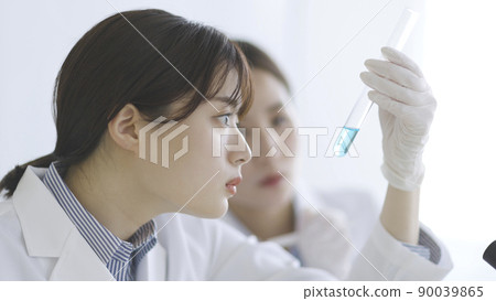 A woman in a white coat staring at a test tube 90039865