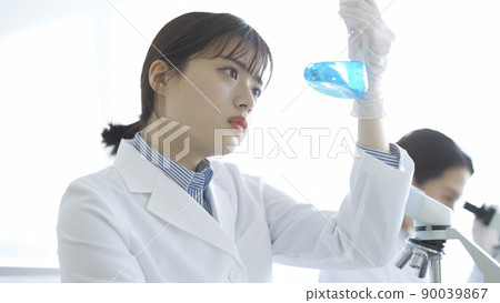 A woman in a white coat staring at a flask Research experiment 90039867