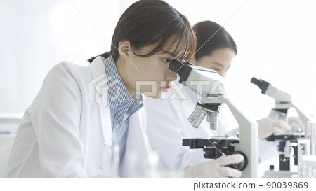 A woman in a white coat looking through a microscope A woman in a white coat looking through a microscope 90039869