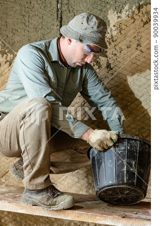 Black bucket with liquid mortar for the first layer of plaster for the wall. Black bucket with liquid mortar for the first layer of plaster for the wall. 90039934
