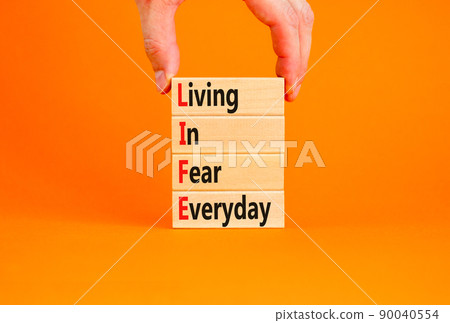 LIFE living in fear everyday symbol. Concept words LIFE living in fear everyday on wooden blocks on an orange background. Businessman hand. Business LIFE living in fear everyday concept. Copy space. 90040554