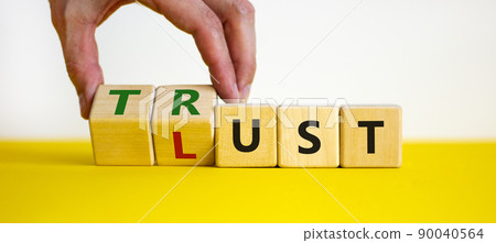 Lust or trust symbol. Businessman turns wooden cubes and changes the words 'lust' to 'trust'. Beautiful yellow table, white background. Business and lust or trust concept, copy space. Lust or trust symbol. Businessman turns wooden cubes and changes the words 'lust' to 'trust'. Beautiful yellow table, white background. Business and lust or trust concept, copy space. 90040564