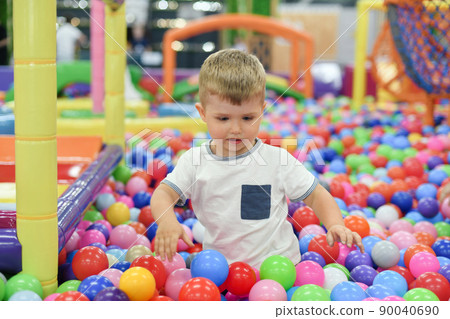 A boy in a dry paddling pool in playing centre with plastic balls. 90040690