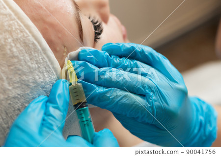 Syringe with a patient's blood plasma in a cosmetologist's hand for a plasmolifting of a woman's facial skin. Plasma therapy, skin cell restoration. 90041756