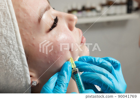Syringe with a patient's blood plasma in a cosmetologist's hand for a plasmolifting of a woman's facial skin. Plasma therapy, skin cell restoration. 90041769