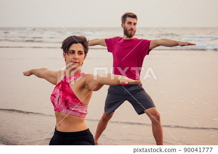 Young sportive couple girl and boy are practicing acroyoga exercises in the sunset on the beach 90041777