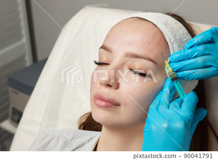 Syringe with a patient's blood plasma in a cosmetologist's hand for a plasmolifting of a woman's facial skin. Plasma therapy, skin cell restoration. 90041791