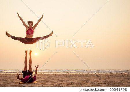 Two people practicing yoga in the sunset light on goa india beach. female and male acro yogi tantra flying copyspce 90041798