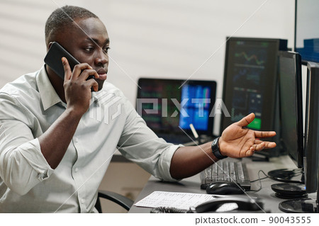 Young African American man working with stock trading stats having phone call with dissatisfied client Young African American man working with stock trading stats having phone call with dissatisfied client 90043555