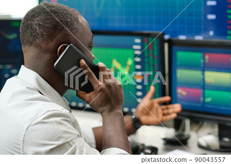 Young Black man working with stock trading stats having phone call with his colleague or client 90043557