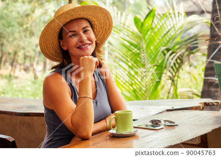 Technology and travel. Working outdoors. Freelance concept. Pretty young woman in hat using laptop in cafe on tropical beach.Hooray victory success and successful deal concept promotion at work 90045763