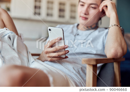 Asian guy sitting at his flat while using mobile phone 90046668