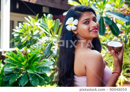 indian woman applying coconut oil dark brunette long hair in a hand on green summer park nature tropical 90048059