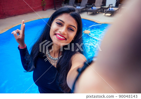 beautiful indian woman toothy white smile selfie portrait on smartphone camera summer cafe by sea by the swimming pool goa 90048143