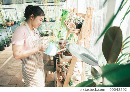 Young woman plant owner shop watering plants in a plant shop. 90048292